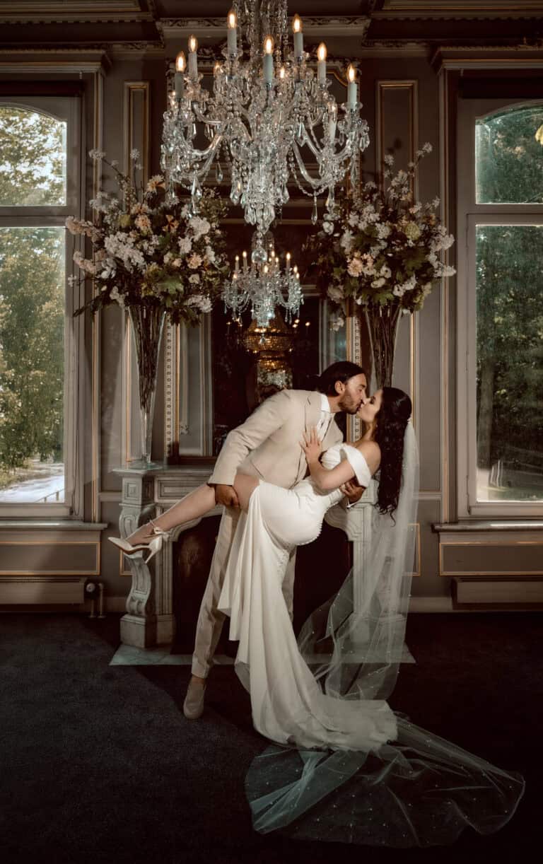 Huwelijkspaar danst onder chandelier in elegante trouwzaal met bloemen decor.
