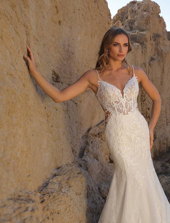 Honeymoonshop trouwjurk Goddess Azuree aan zee met rotsen en water.