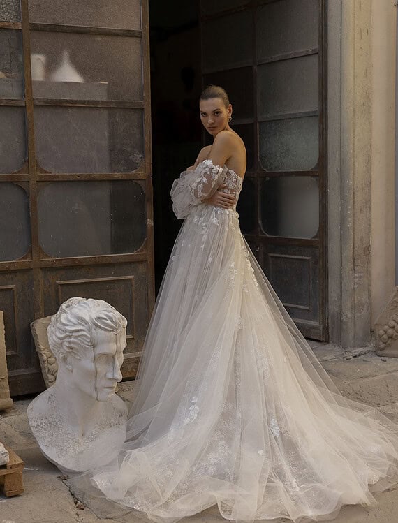 Bruidsjurk met lange sleep, kantdetails en elegante uitstraling.