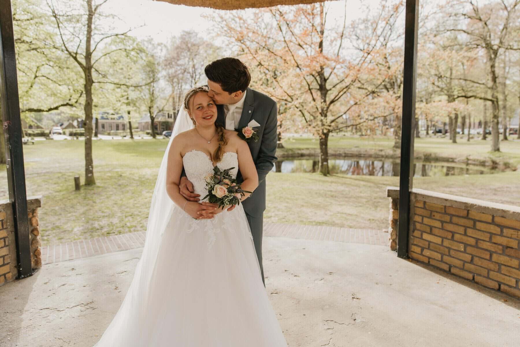 Liefdevol bruidspaar op trouwlocatie in park, romantisch huwelijksfoto.